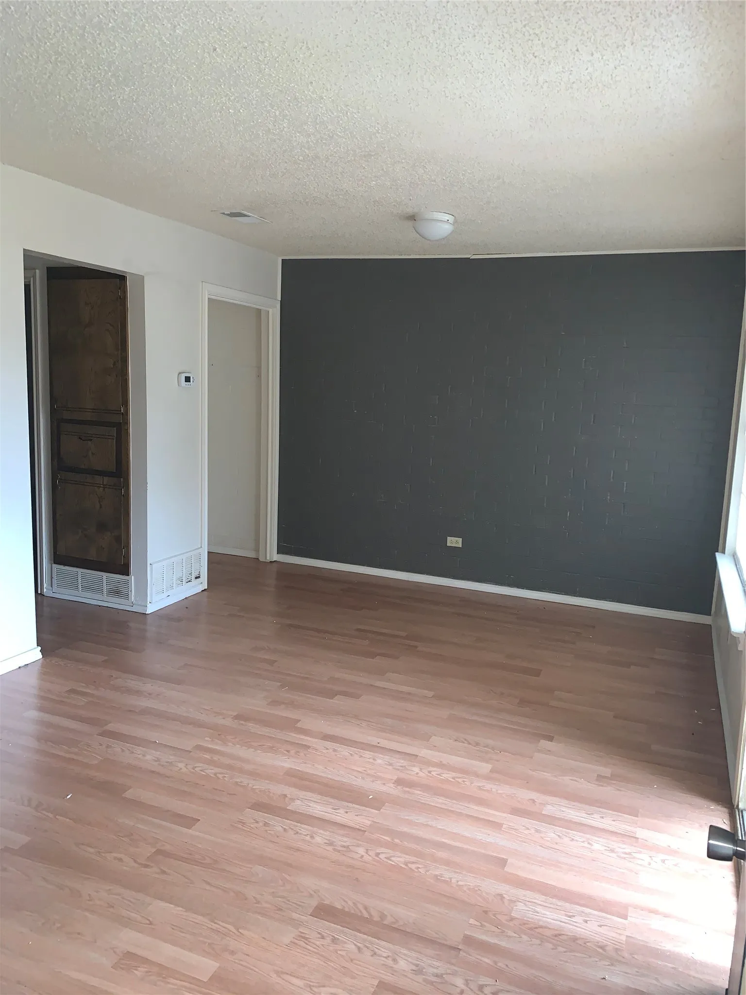Spacious room featuring wood-finish flooring, a textured accent wall, and a built-in architectural element with decorative grating