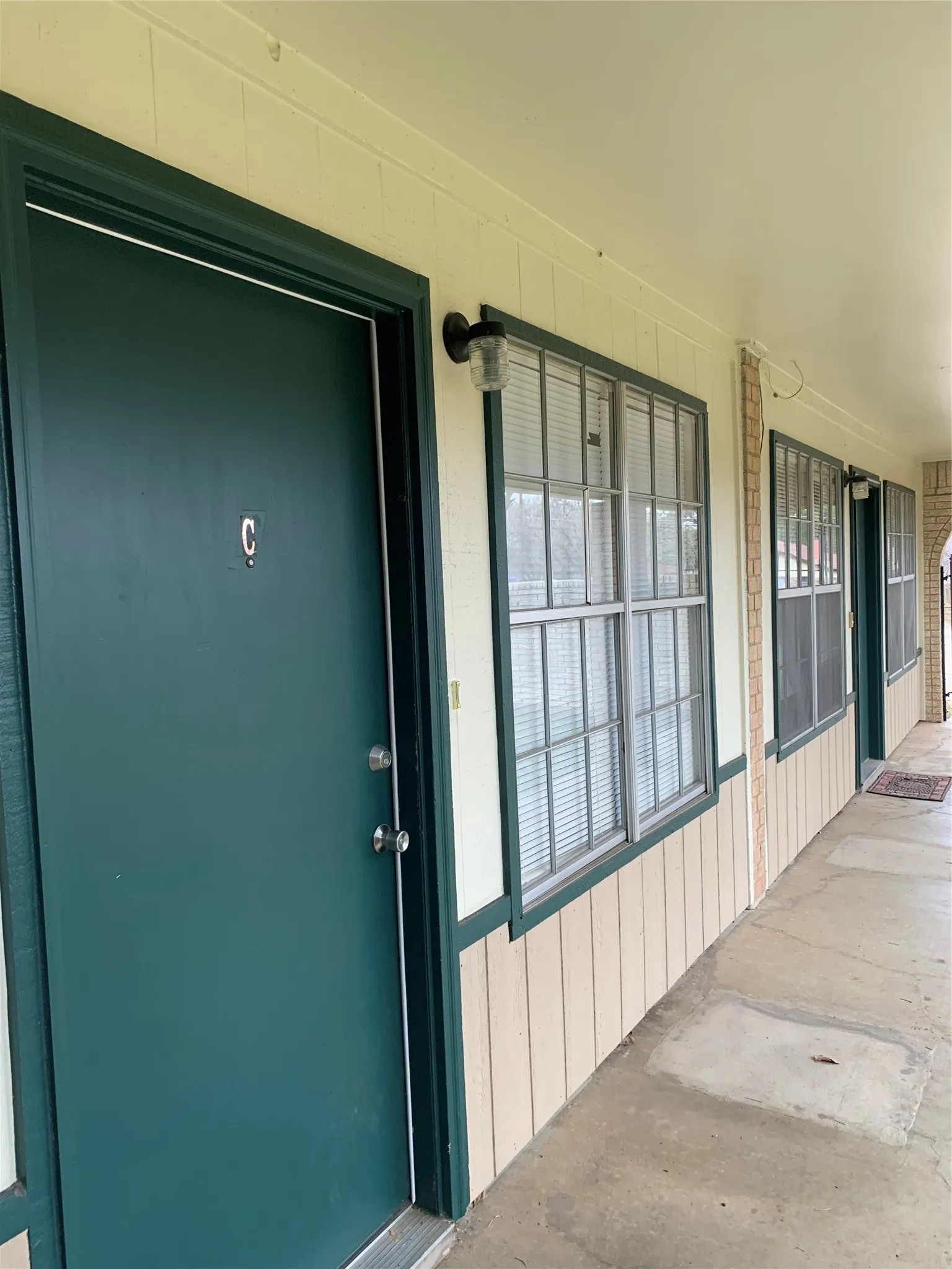 Exterior corridor with a dark green entry door, white trim, and a wall-mounted light fixture