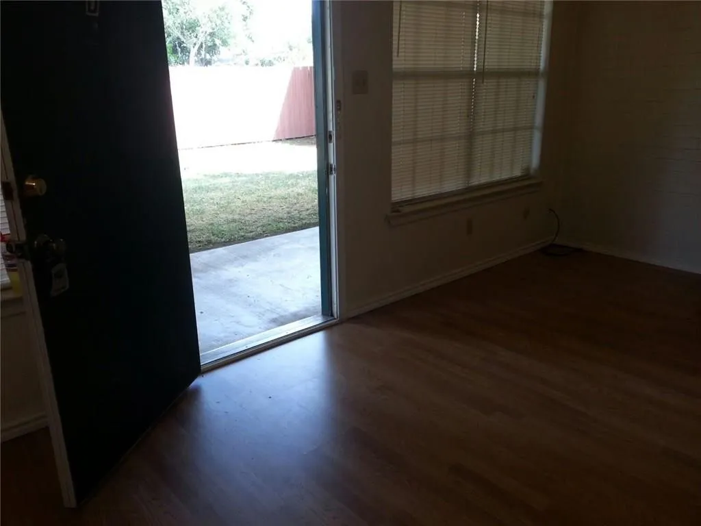 Interior space featuring wood-finish flooring, a large window with blinds, and a rear door opening to an outdoor patio and grass area