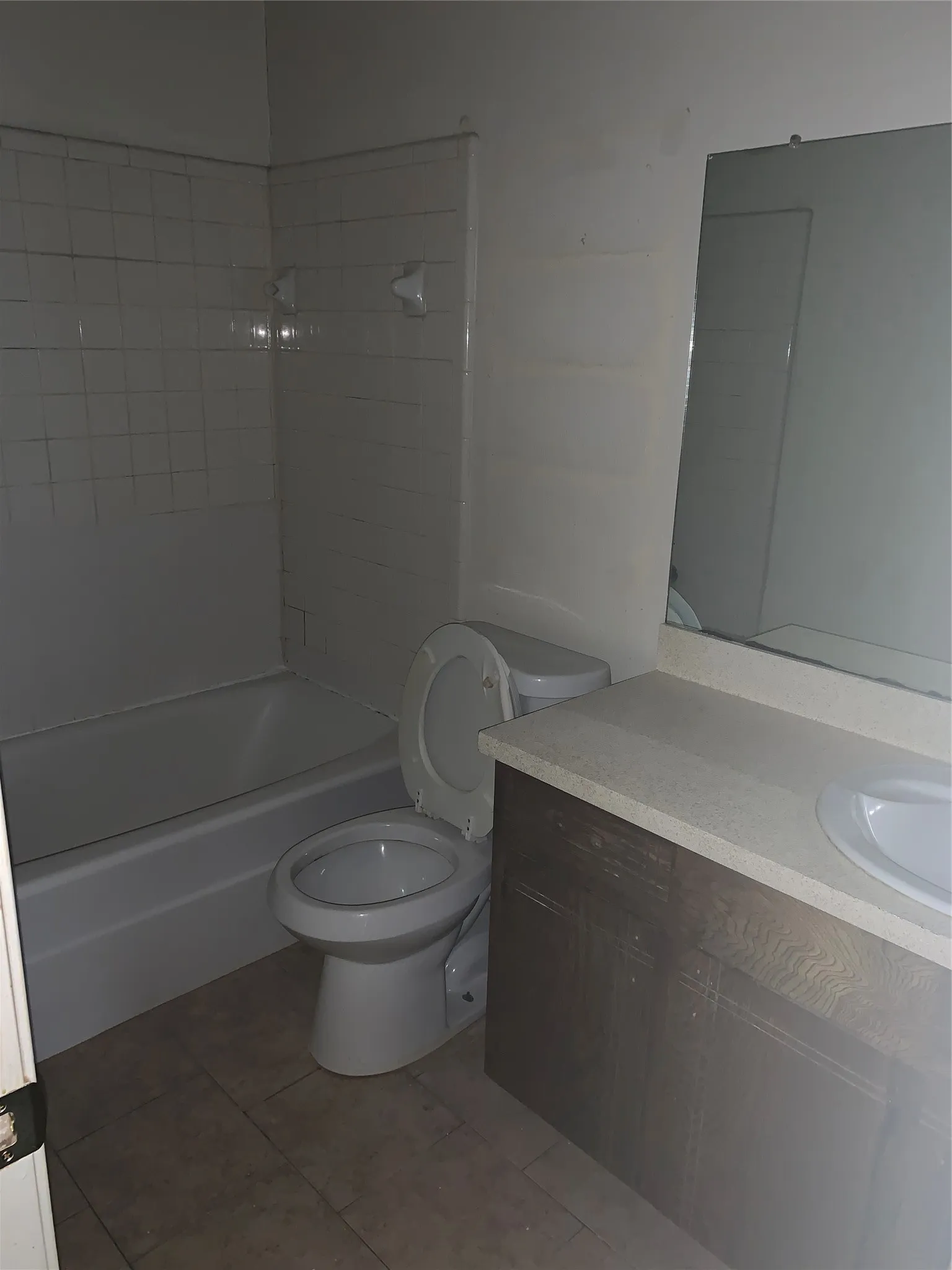 Bathroom featuring a white bathtub with tile surround, toilet, and a vanity with a light-colored countertop and integrated sink