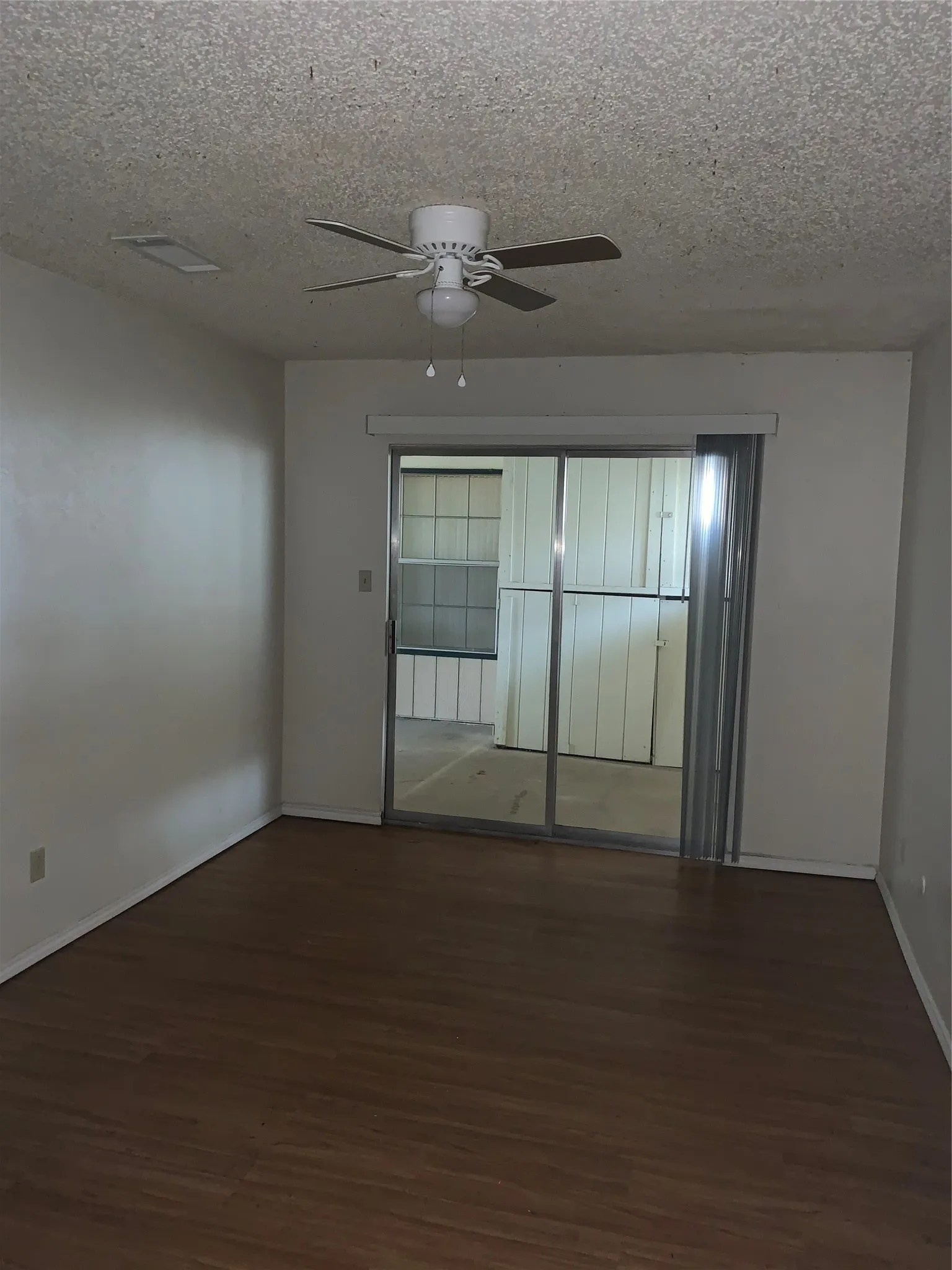 Living area with wood-finish flooring, a ceiling fan, and sliding glass doors opening to an enclosed patio