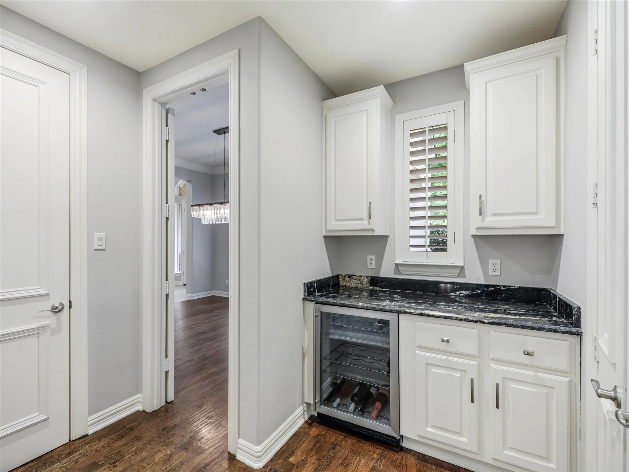 Built-in wet bar featuring white cabinetry, dark stone countertop, and an integrated beverage refrigerator