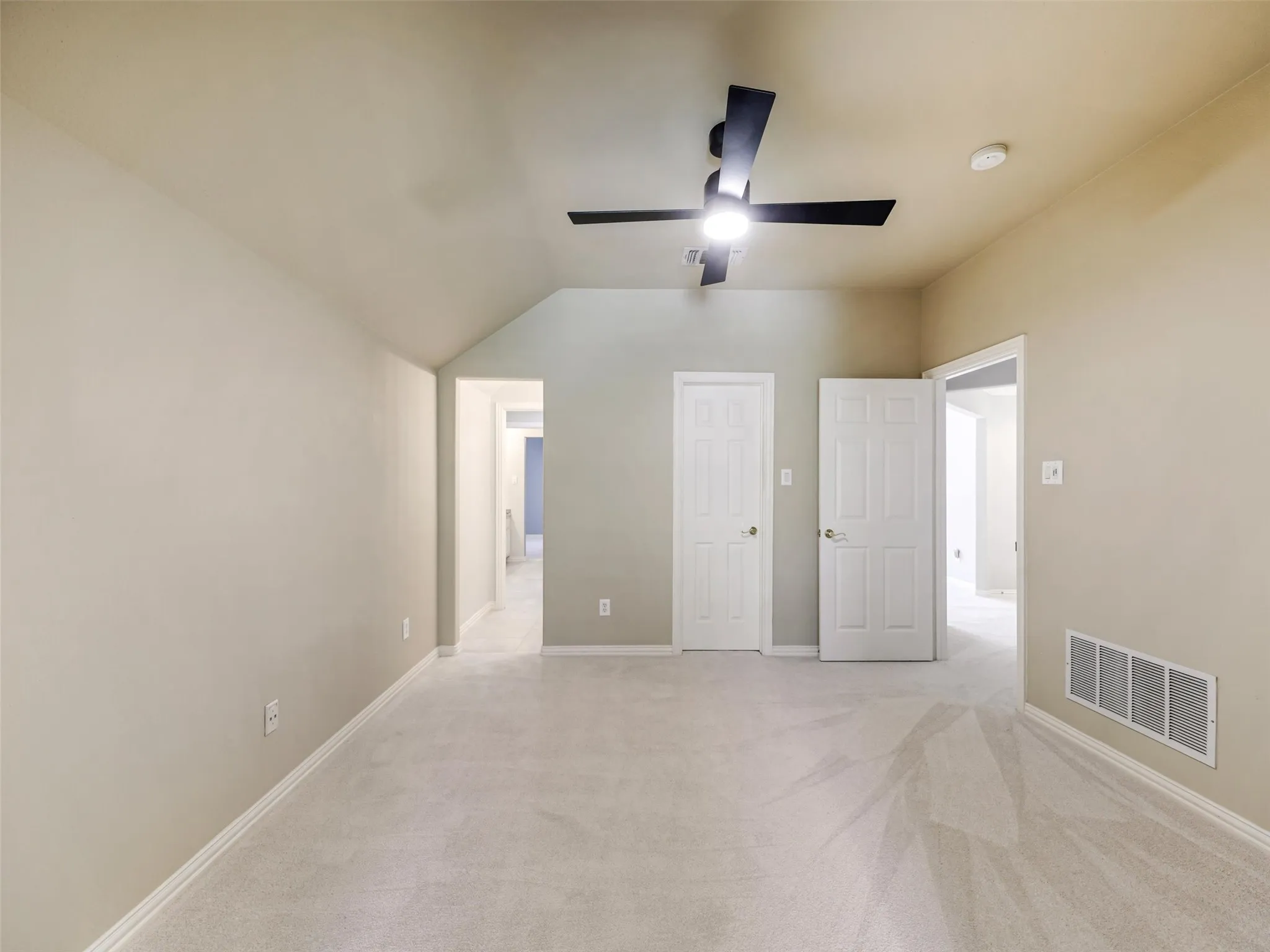 Vaulted ceiling with a ceiling fan, neutral wall paint, light-colored carpeting, and white interior doors