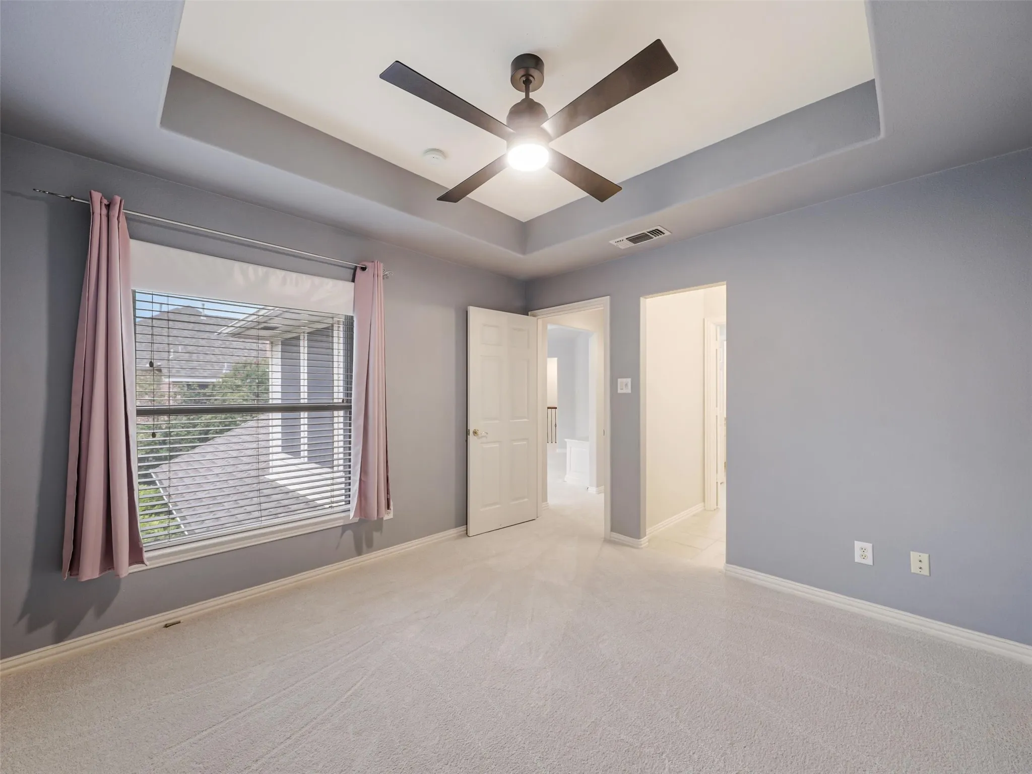 Tray ceiling with a ceiling fan light fixture, carpeted flooring, and a window with blinds