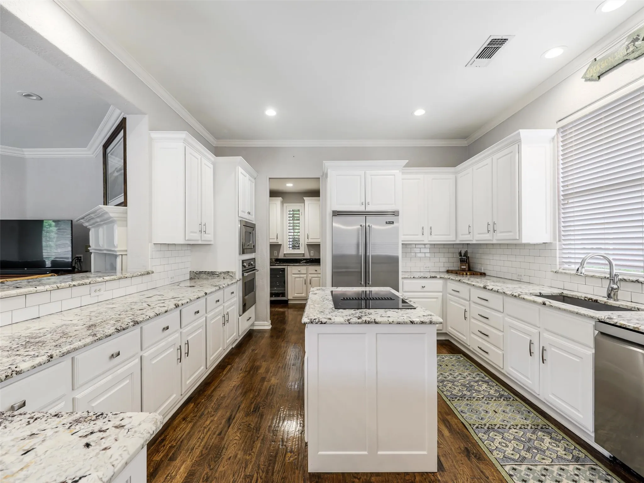 Chef's kitchen featuring white shaker cabinetry, speckled countertops, subway tile backsplash, stainless steel appliances, and a central island with a built-in cooktop