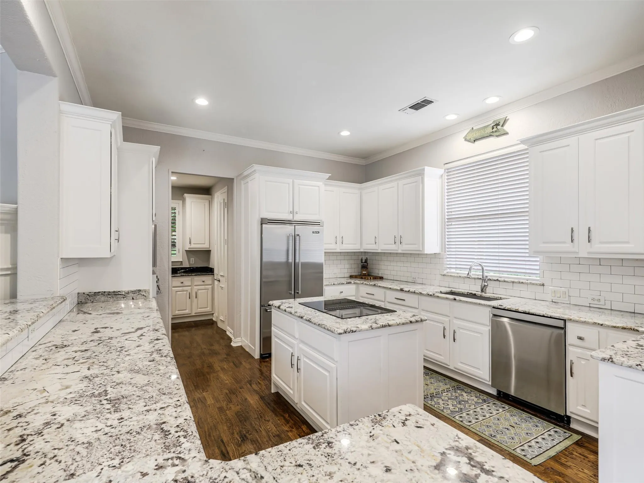 Spacious kitchen featuring white cabinetry, light-toned countertops, stainless steel appliances, a center island with a cooktop, and wood-finish flooring