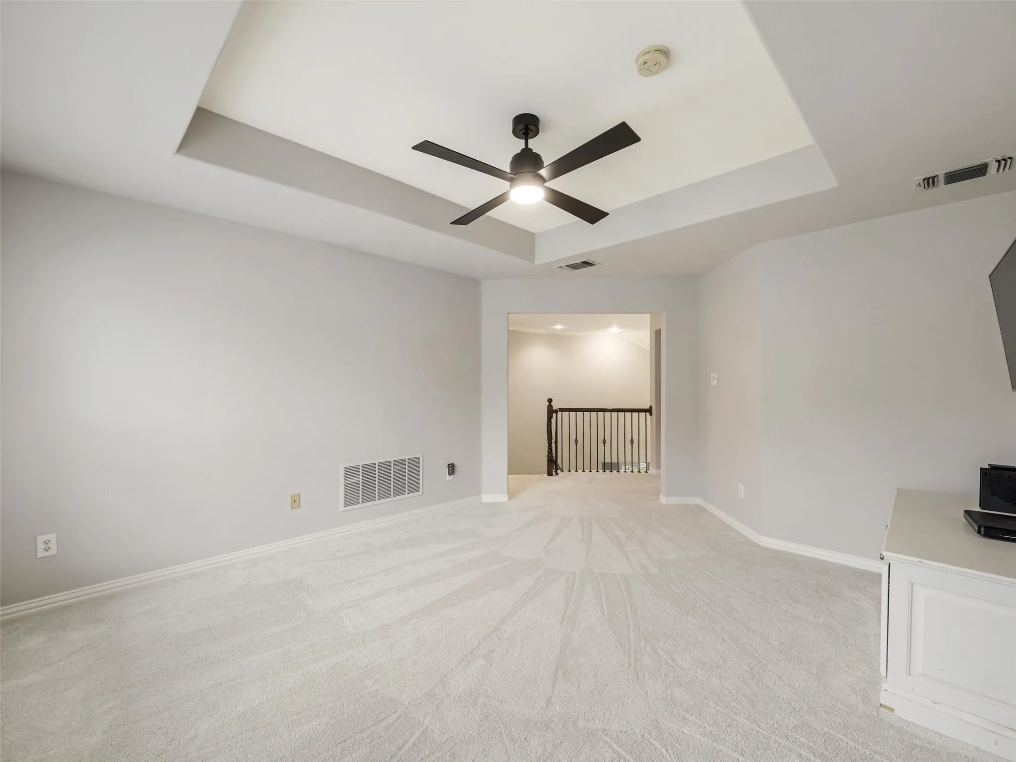 Tray ceiling with a black ceiling fan, light gray wall paint, and light-colored carpeting