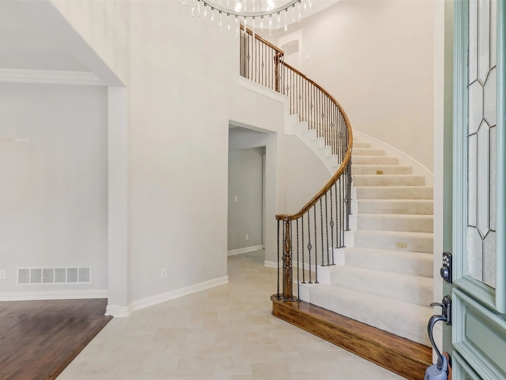 Grand entryway featuring a curved staircase, wrought iron balusters, a large chandelier, tile flooring, and wood-finish flooring