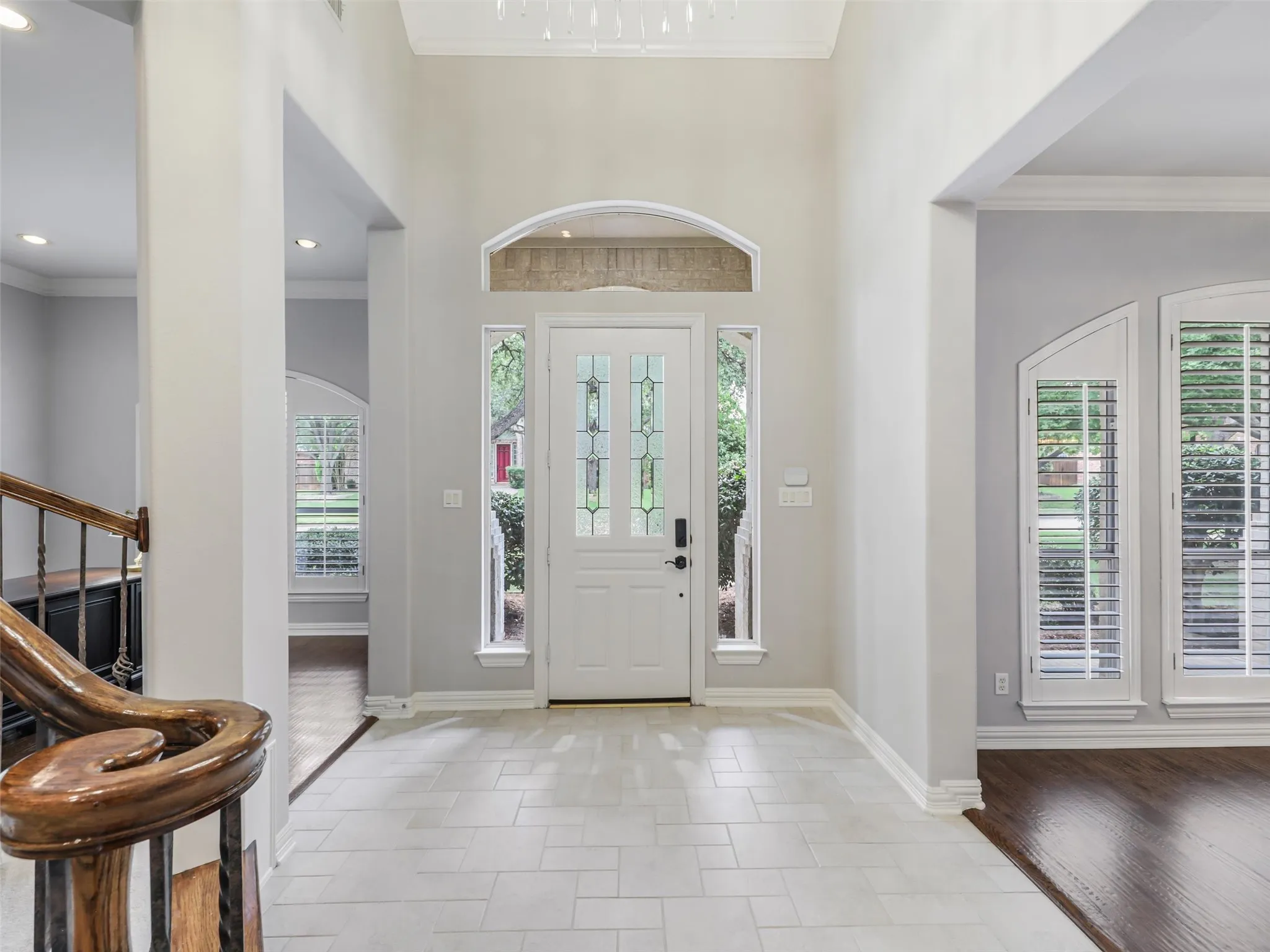 Two-story foyer with white tile flooring, a decorative front entry door with leaded glass, side lights, and transom window, and an adjacent staircase with wood railings