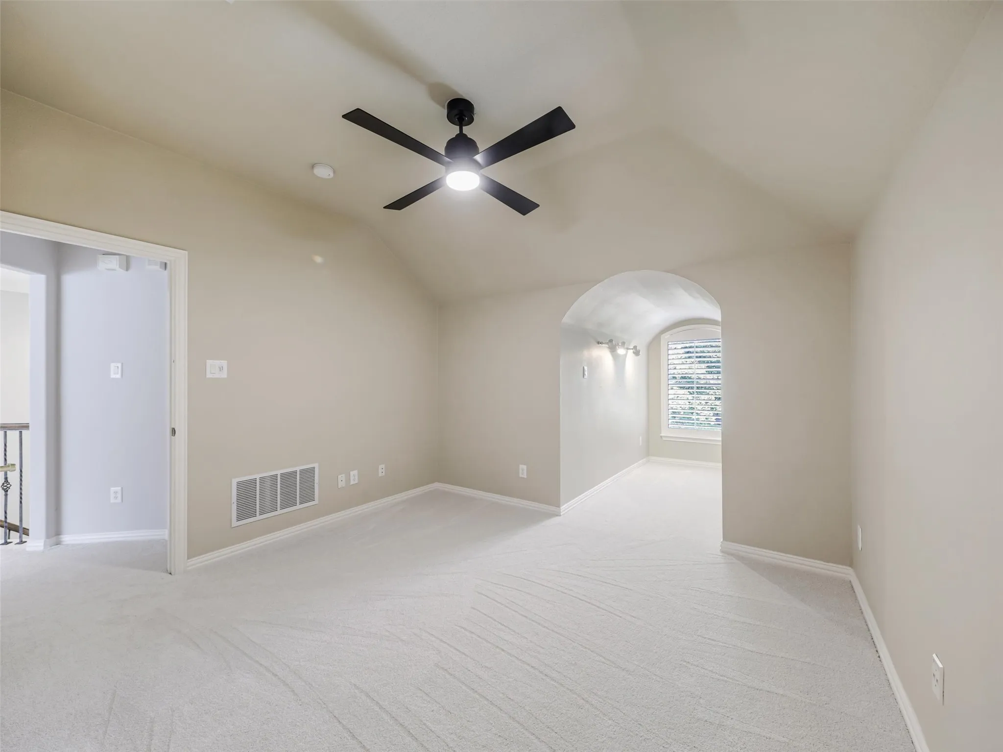 Vaulted ceiling with a black-finish ceiling fan, recessed lighting, light-colored carpet flooring, arched hallway, and an arched window with blinds