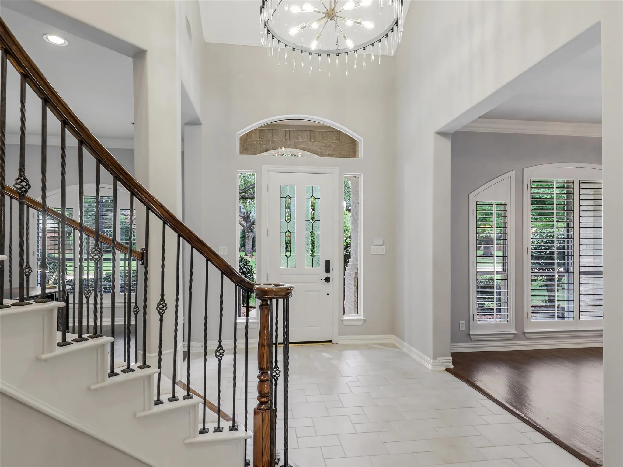 Two-story foyer with a decorative chandelier, tile flooring, and a grand staircase featuring wrought iron balusters