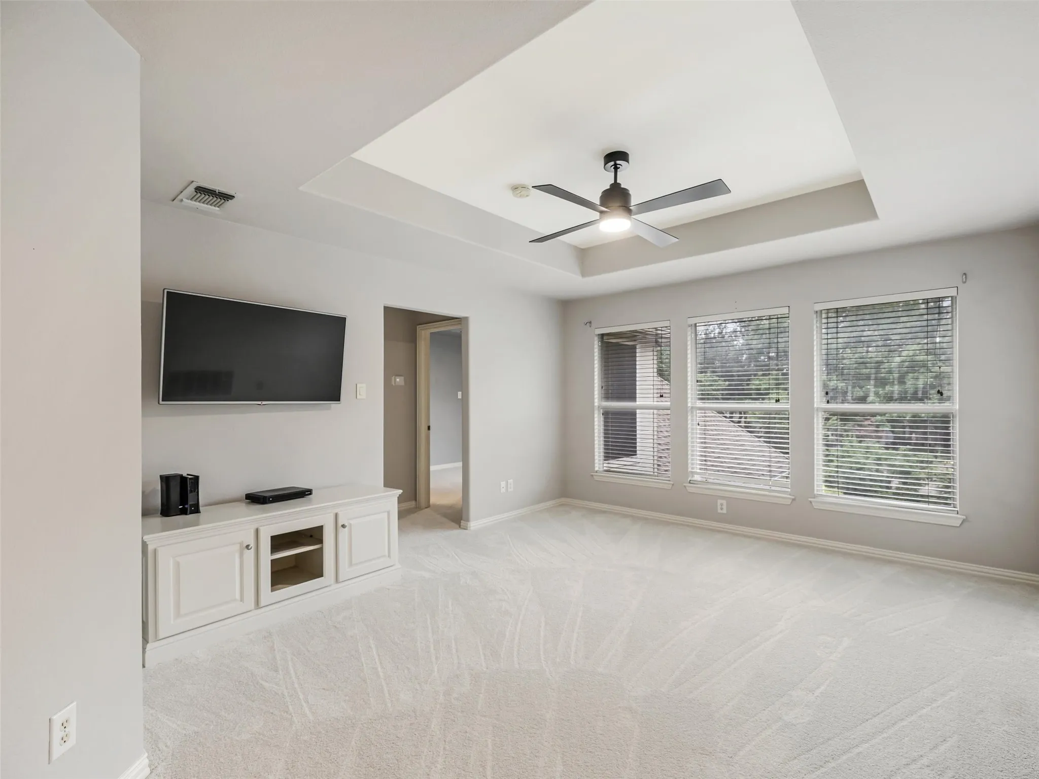 Recessed ceiling with a flush-mount ceiling fan, three paneled windows with blinds, and light-toned carpeting