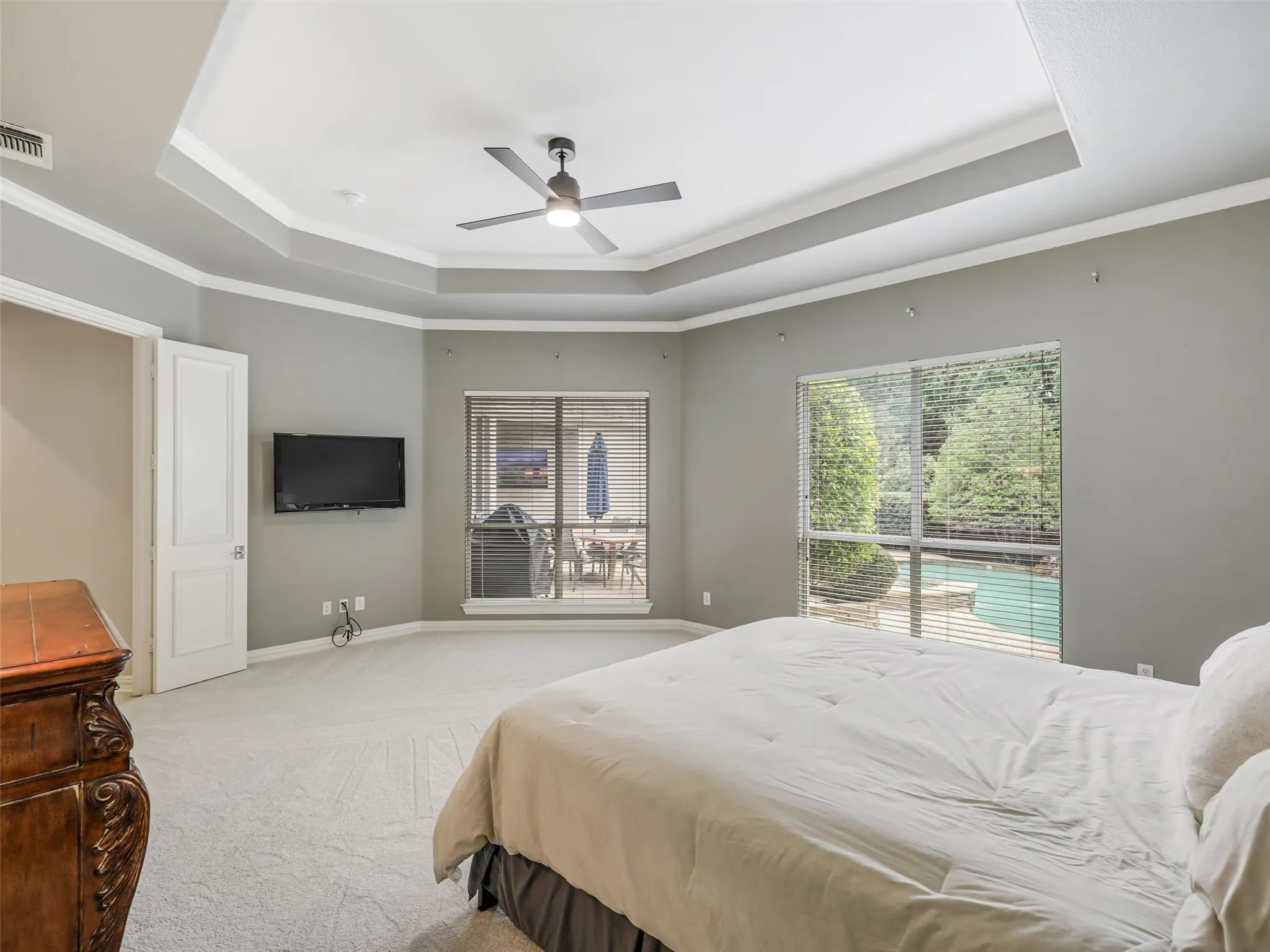 Tray ceiling with crown molding and ceiling fan, wall-mounted television, and carpet flooring