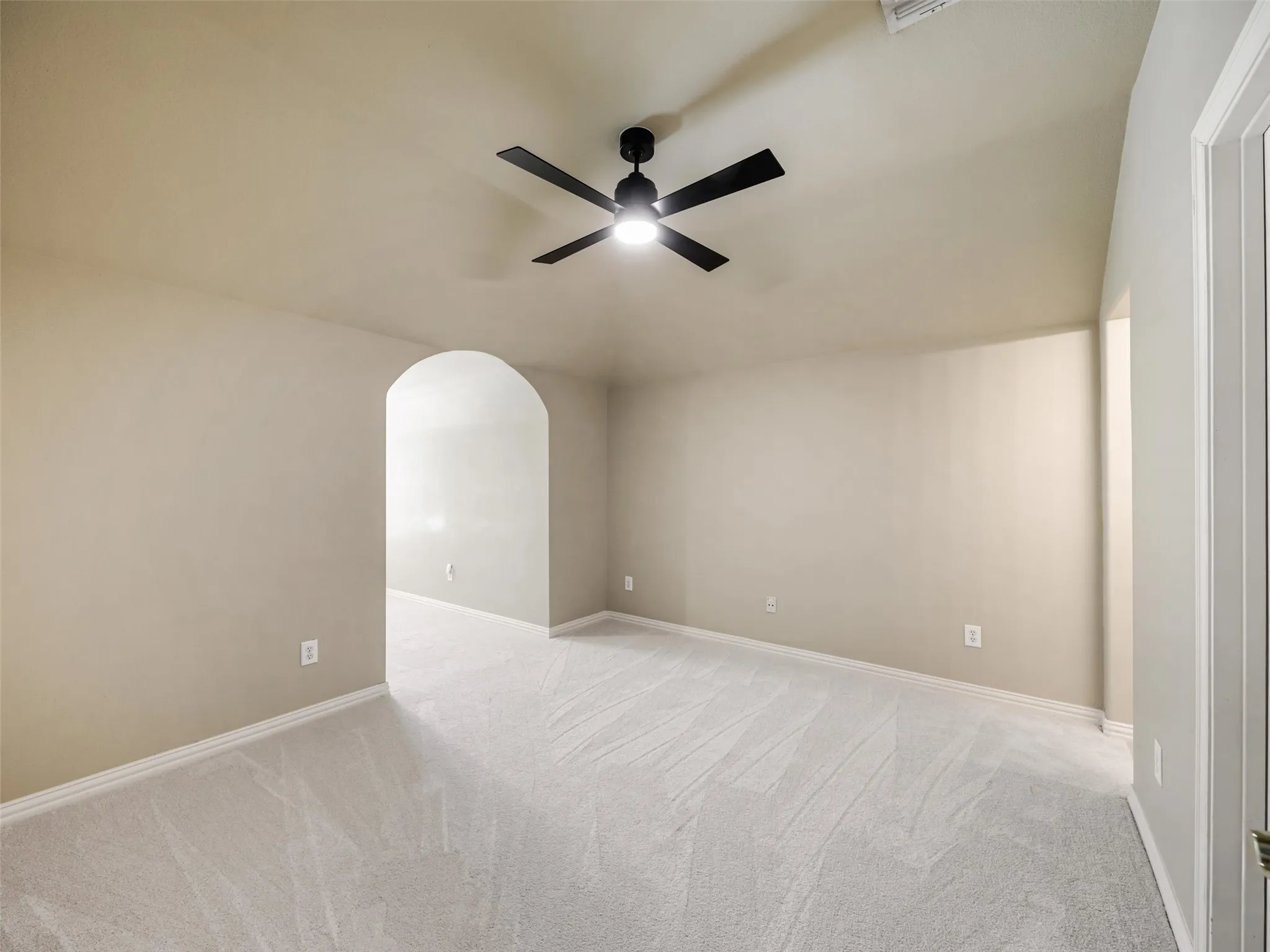 Arched doorway, vaulted ceiling, neutral wall tones, ceiling fan with light, and light-toned carpeting