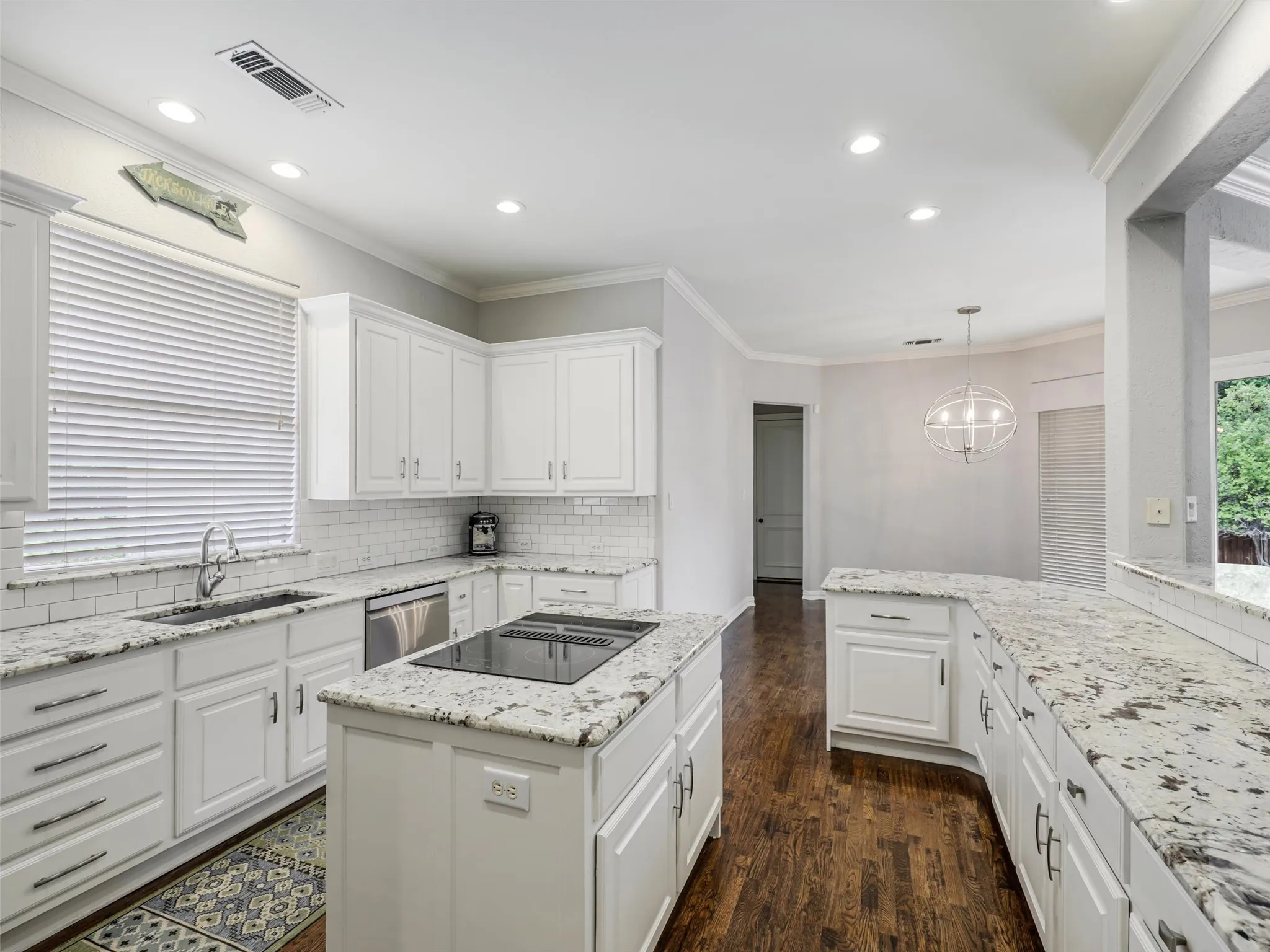 Kitchen featuring white cabinetry, subway tile backsplash, light-toned countertops, a central island with cooktop, and wood-finish flooring