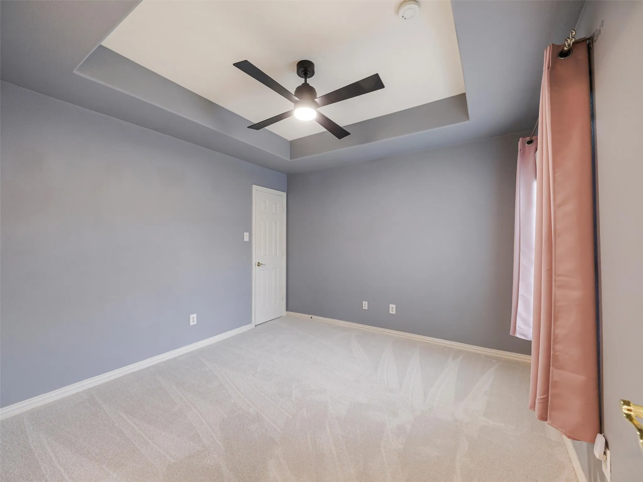 Tray ceiling with a black ceiling fan, light gray wall paint, and light-colored carpeting