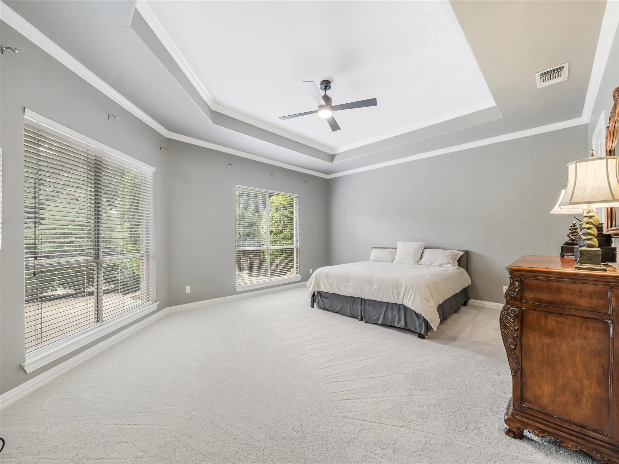 Recessed tray ceiling with crown molding, ceiling fan, and light gray wall paint