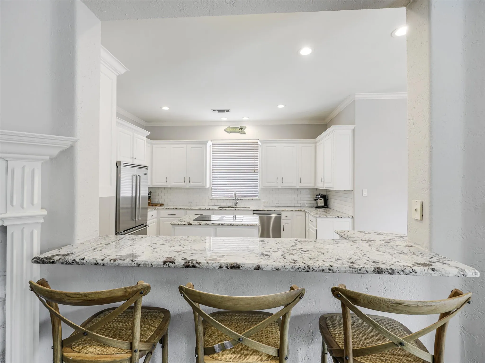 Open kitchen featuring white cabinetry, subway tile backsplash, stainless steel appliances, recessed lighting, and a breakfast bar with stone countertop