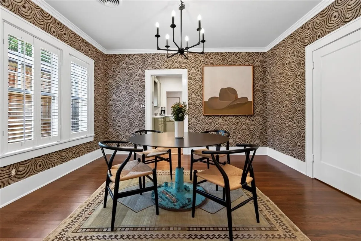 Formal dining room featuring patterned wallpaper, wood-finish flooring, white plantation shutters, crown molding, and a modern chandelier