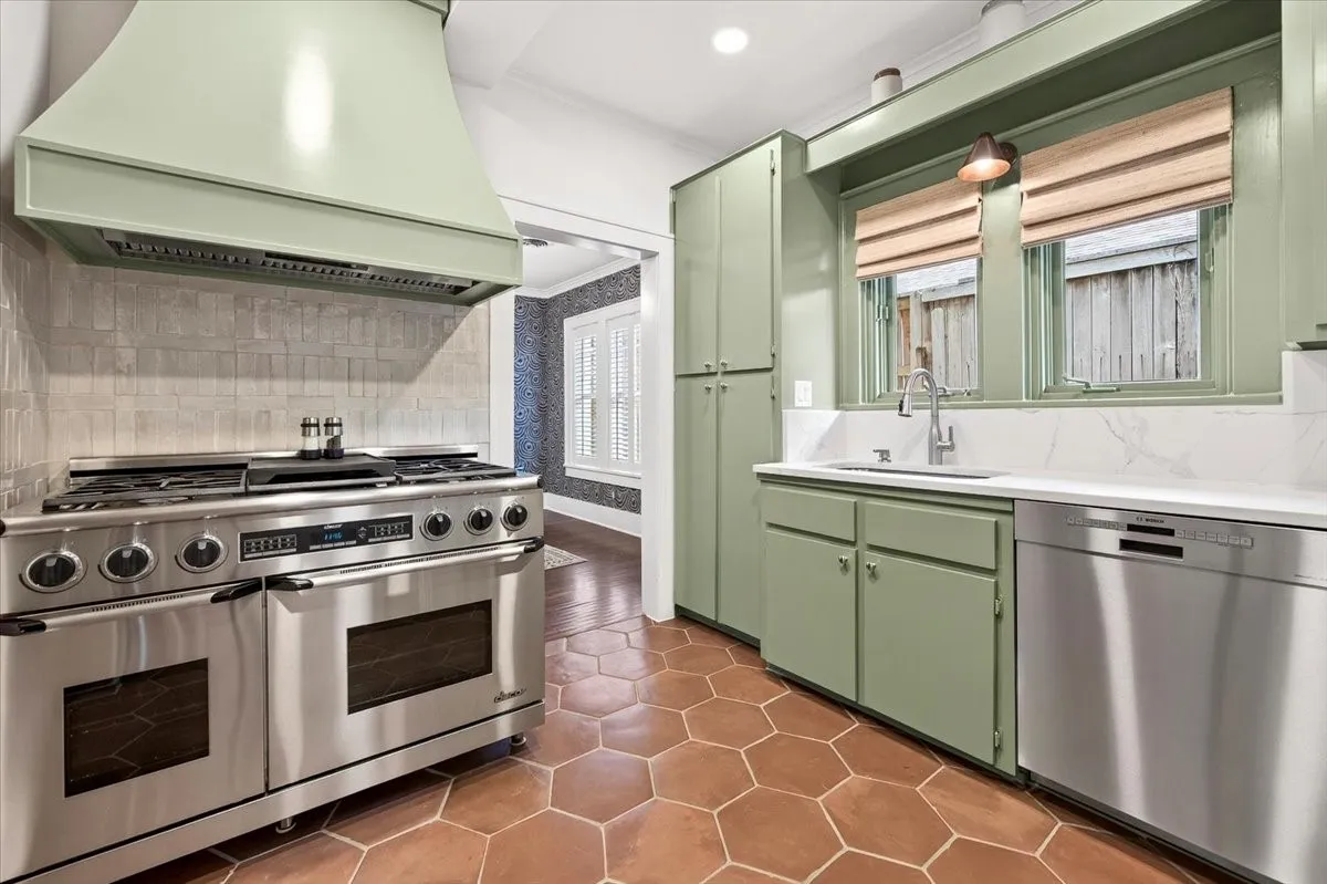 Professional-grade stainless steel range with a custom sage green vent hood, hexagon tile flooring, and ample cabinetry
