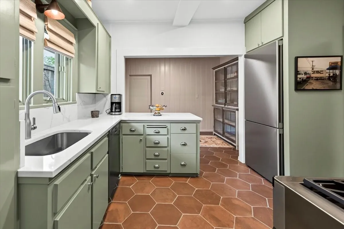 Kitchen featuring hexagonal terra cotta-style flooring, sage green cabinetry, stainless steel appliances, white countertops, and a built-in display cabinet