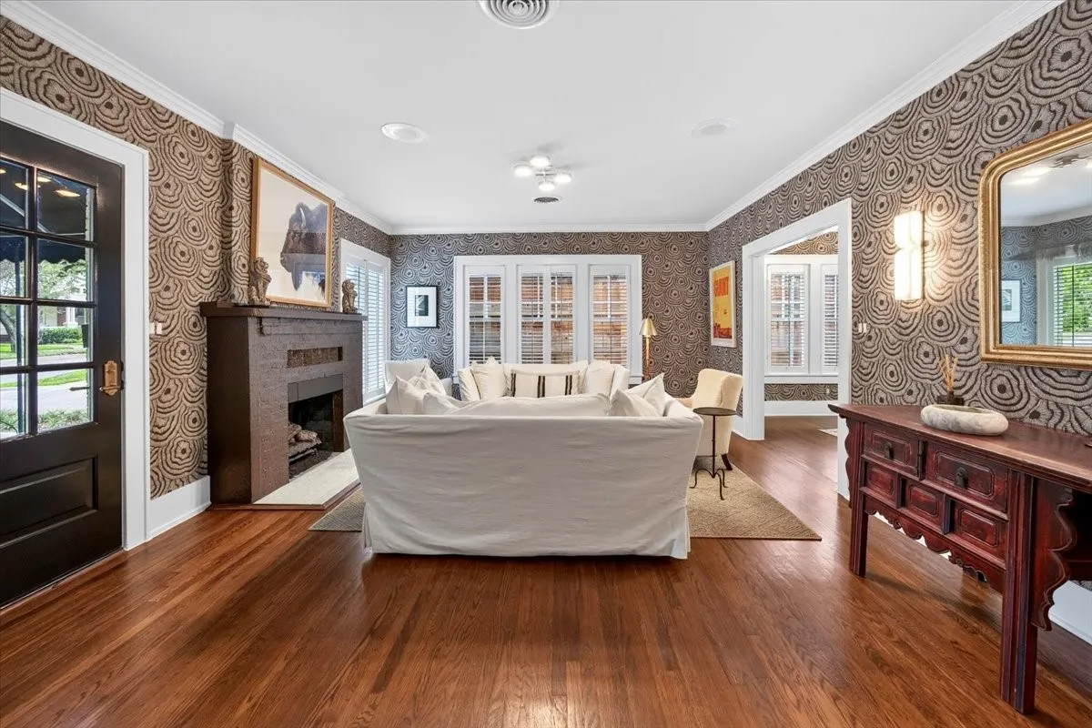 Hardwood flooring throughout featuring a decorative fireplace, crown molding, and intricate patterned wallpaper