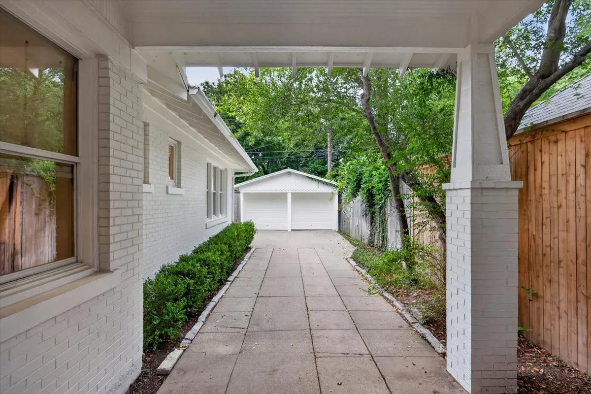 White painted brick exterior with multiple windows, a long concrete driveway, and a detached two-car garage