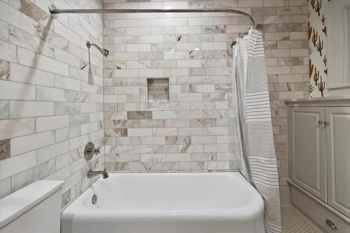 Bathtub with a subway-tiled surround, built-in shower niche, and polished chrome fixtures
