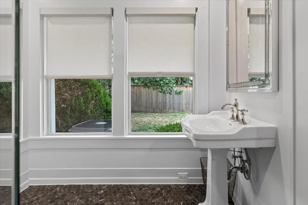 Pedestal sink with polished nickel faucet, set against white wainscoting and dark hexagonal floor tiles