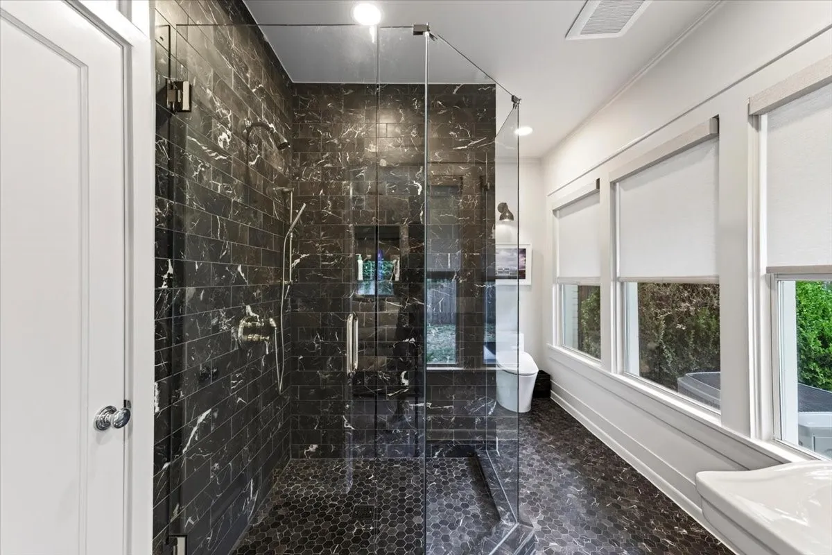 Spacious shower with dark marble-look subway tile walls, a dark hexagonal tile floor, and a clear glass enclosure