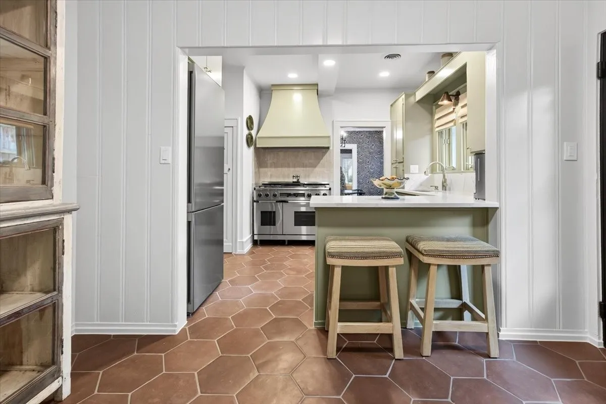 Kitchen featuring hexagonal terracotta-style flooring, a built-in breakfast bar with a solid surface countertop, stainless steel appliances, a custom range hood, and a paneled refrigerator