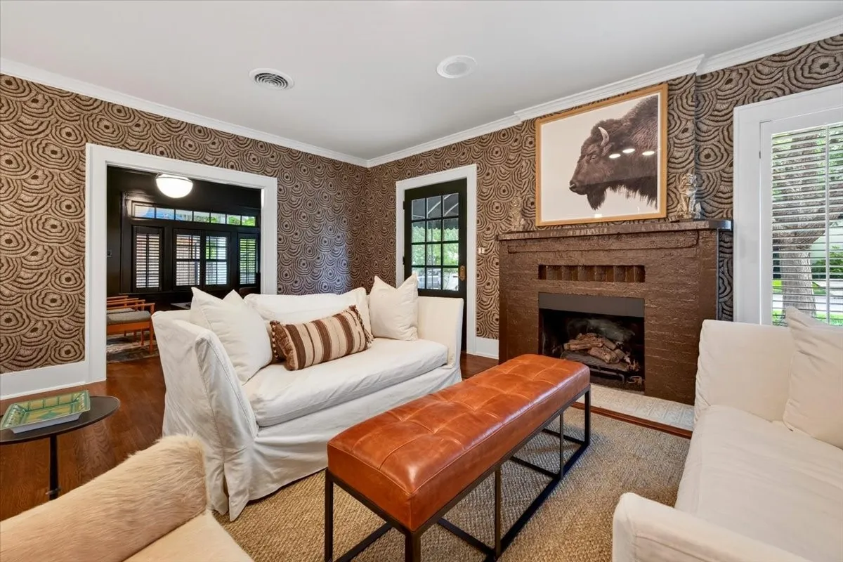 Living room featuring a brick fireplace with a hearth, patterned wallpaper, crown molding, and wood-finish flooring