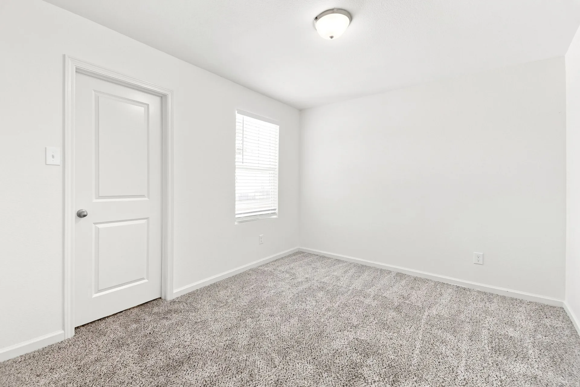 Room featuring light gray textured carpeting, white walls, and a single window with horizontal blinds