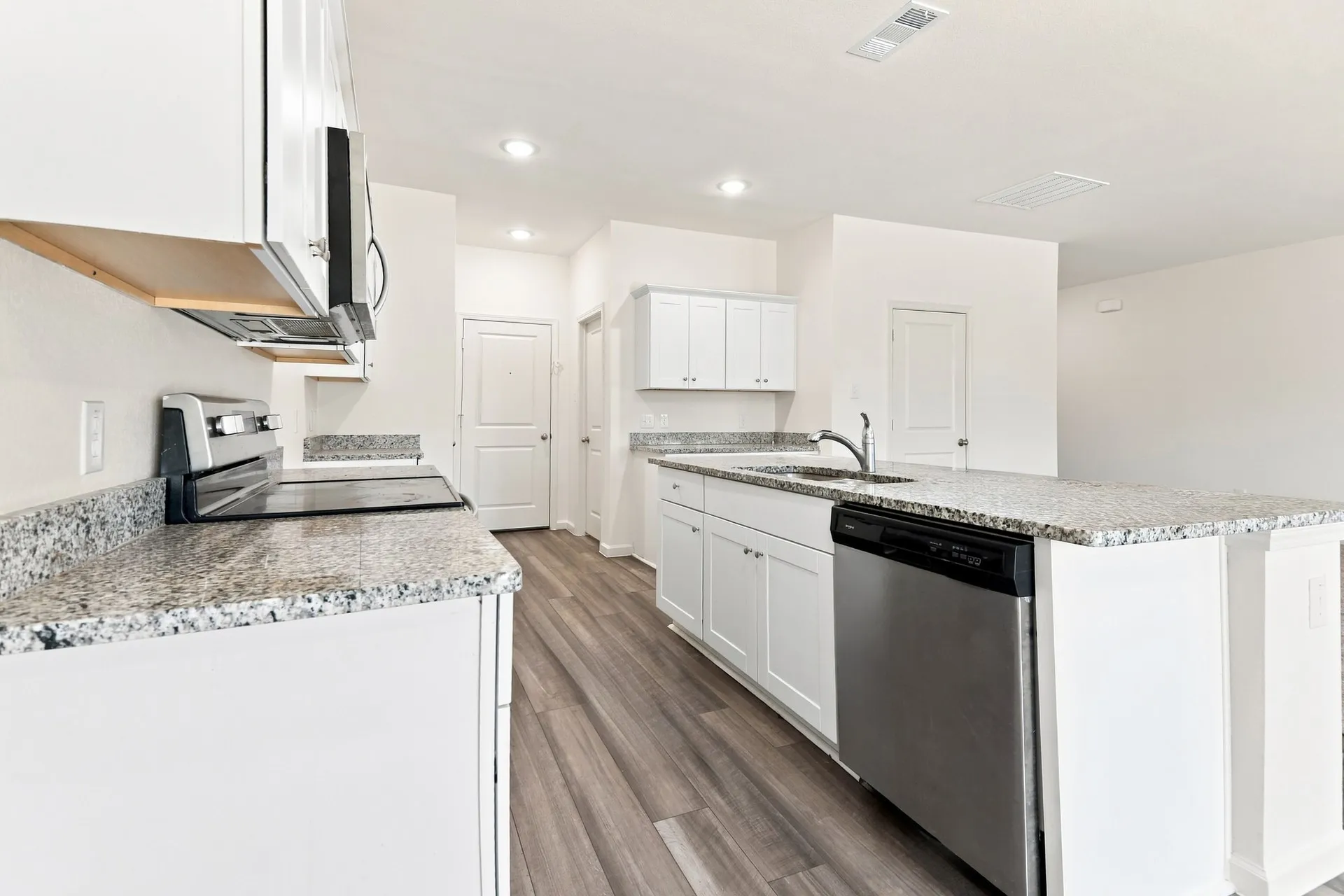Modern kitchen featuring white cabinetry, granite countertops, stainless steel appliances, a kitchen island with a sink, and wood-finish flooring