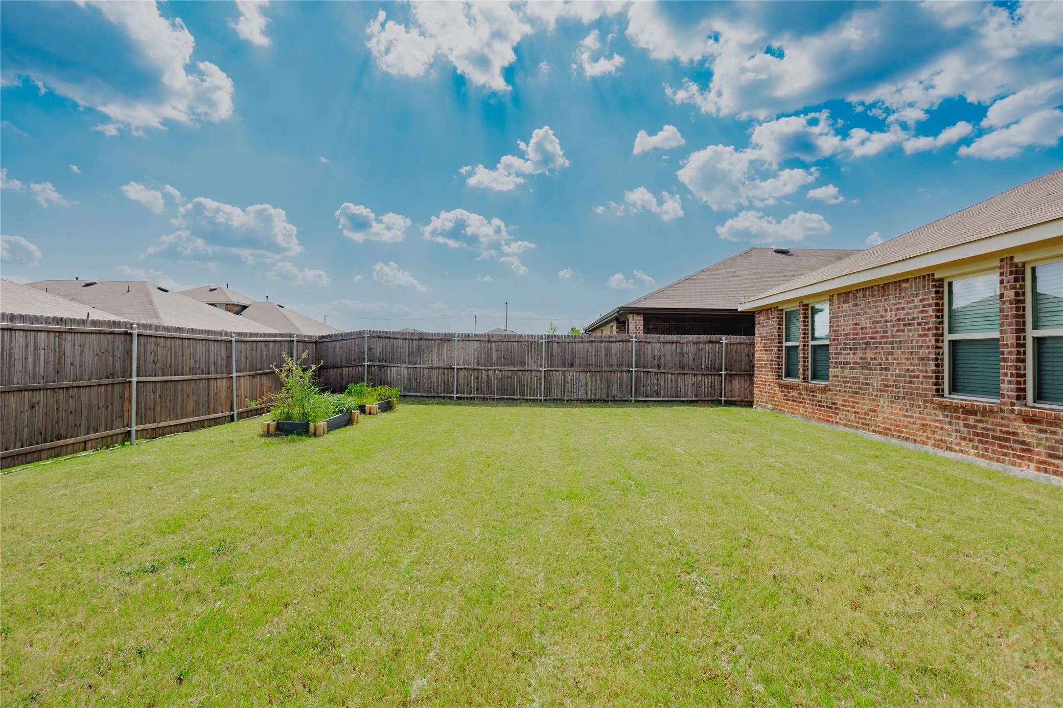 Expansive backyard featuring a green lawn, wood privacy fencing, and raised garden beds