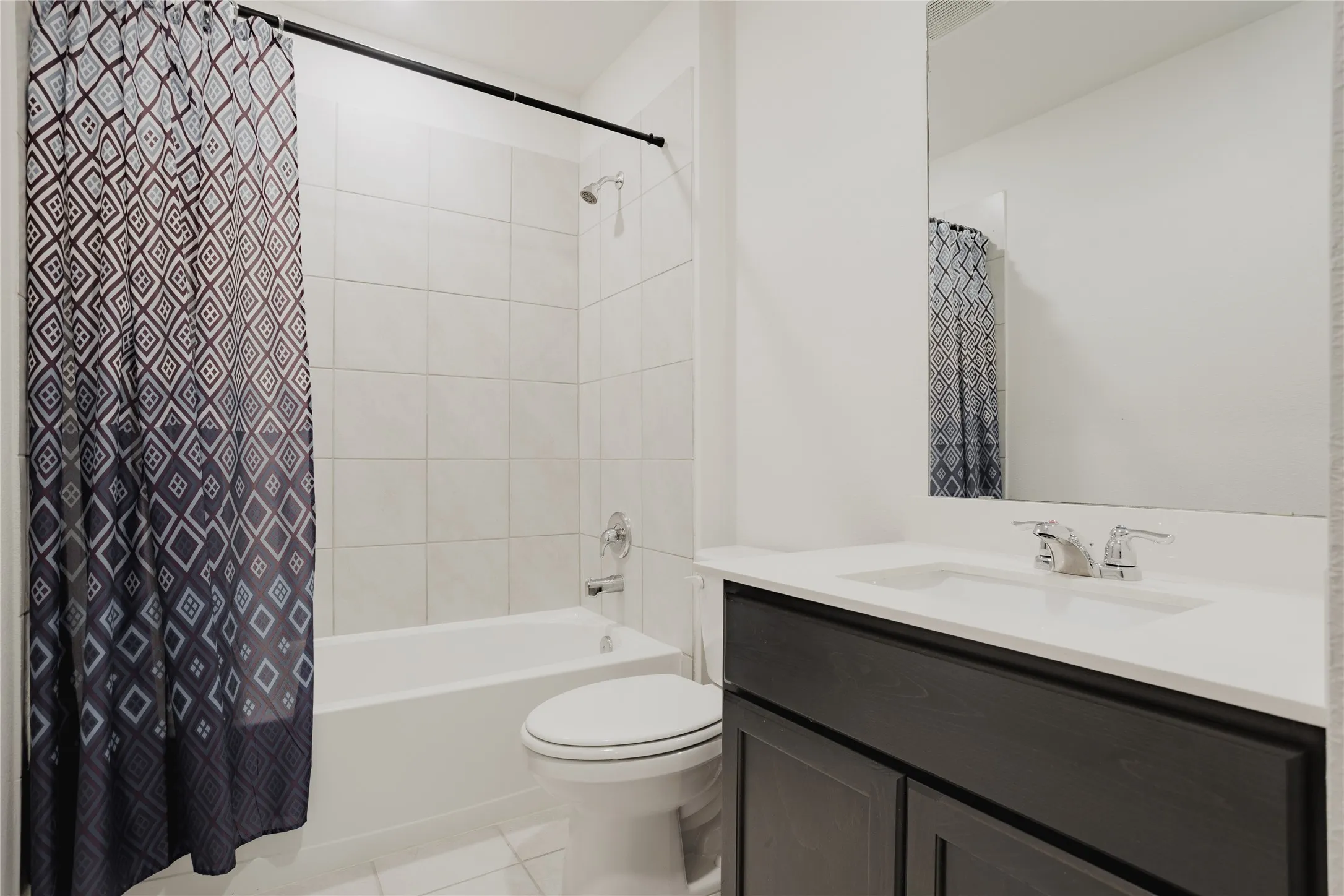 Bathroom featuring a white bathtub, ceramic tile surround, and a dark wood-finish vanity with an integrated sink and chrome fixtures
