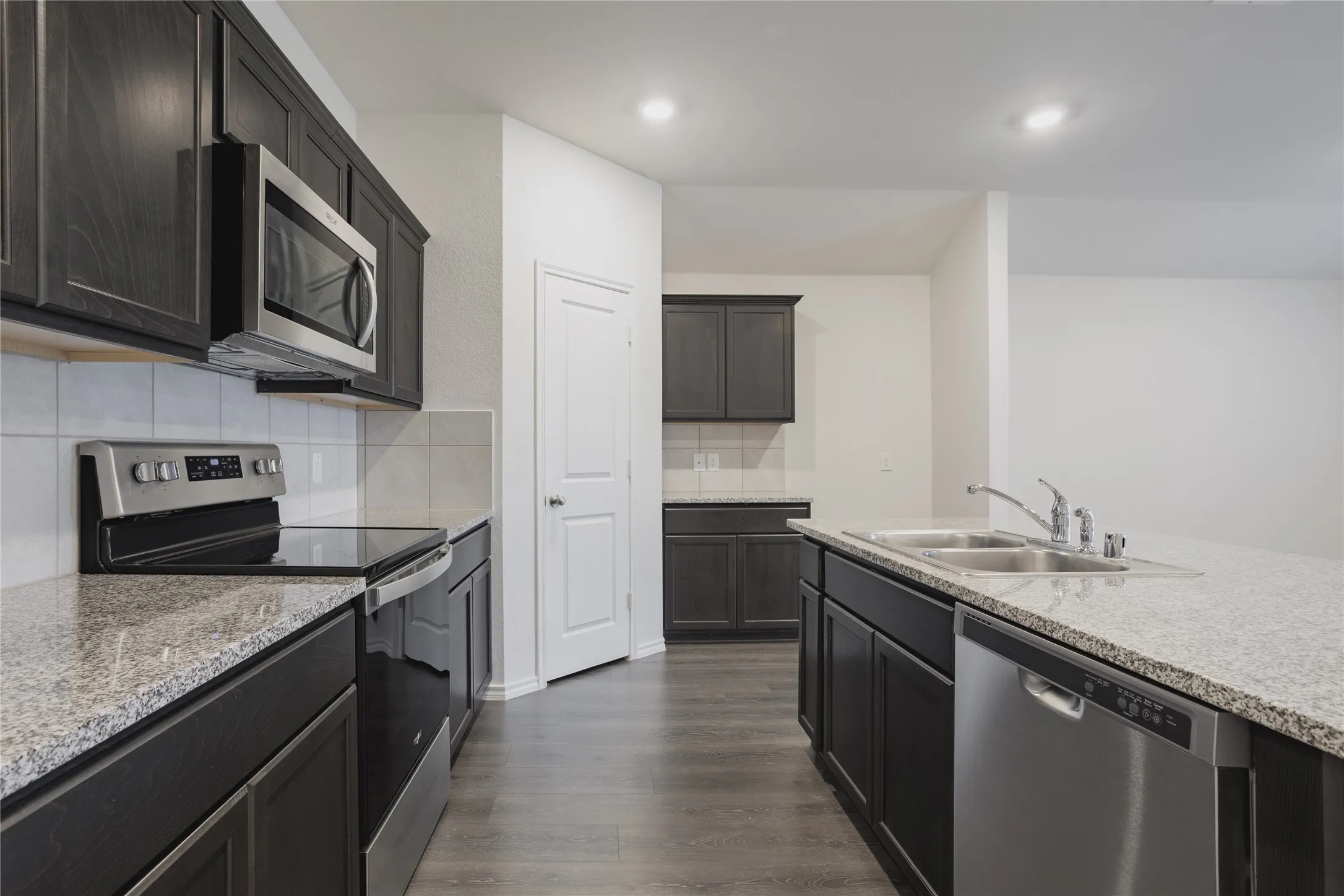 Kitchen with dark wood cabinetry, light speckled countertops, stainless steel appliances, and wood-finish flooring