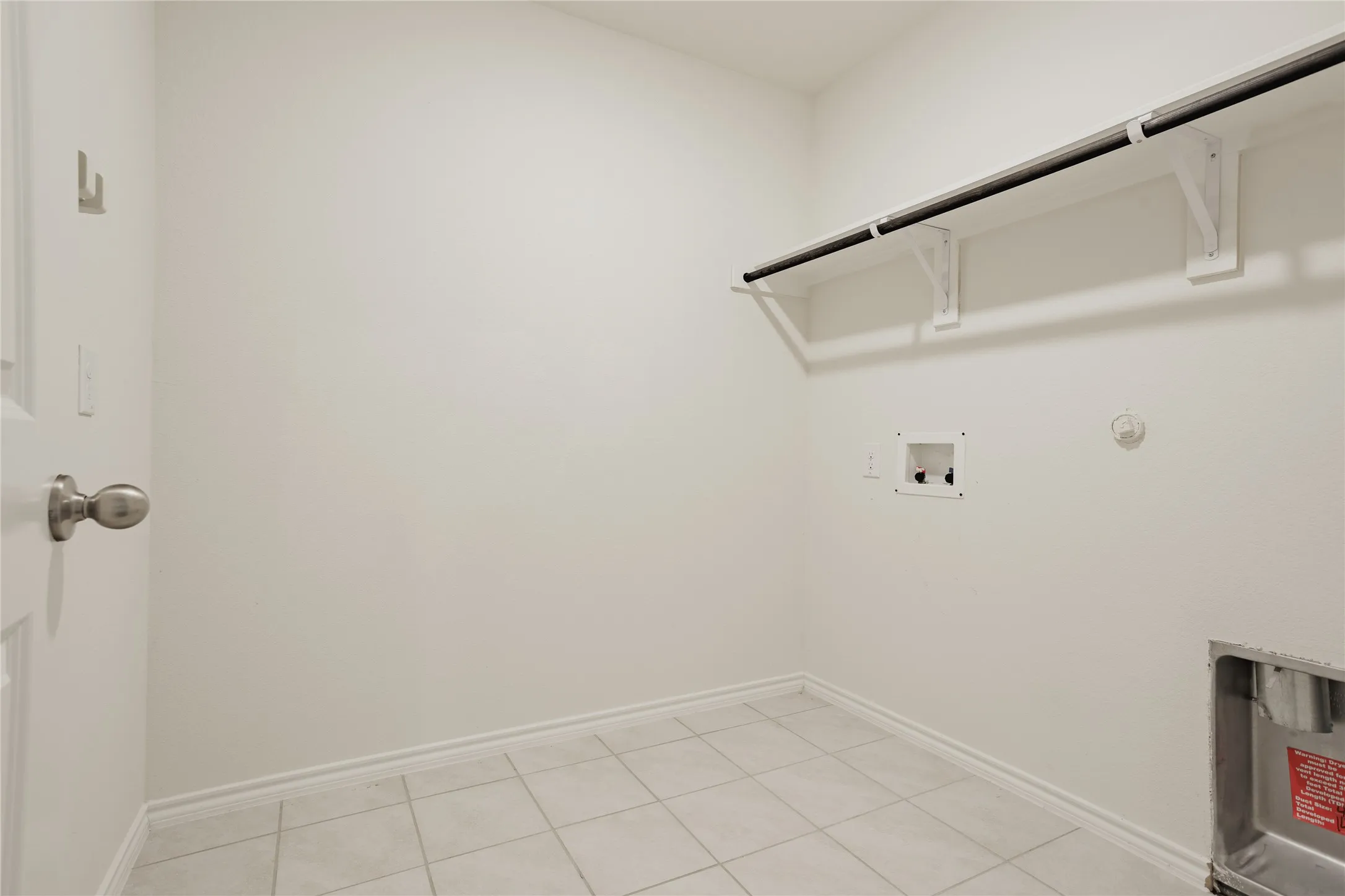Utility room featuring tile flooring, white baseboards, a built-in shelf with a hanging rod, and appliance hookups