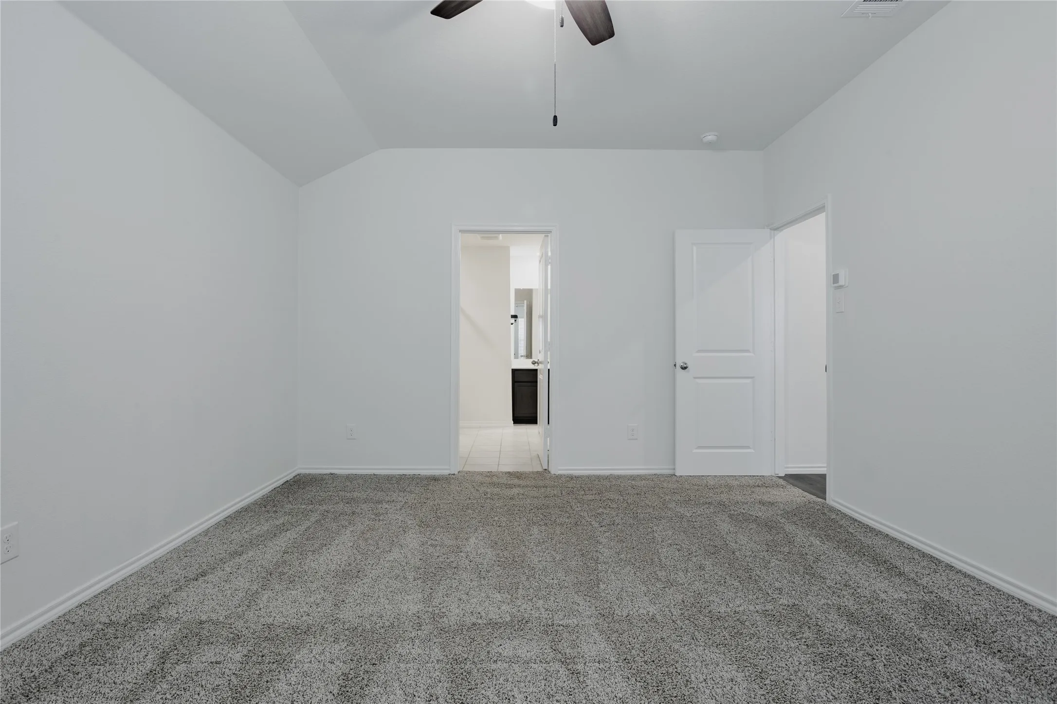 Spacious room featuring gray textured carpet, white baseboards, and a ceiling fan
