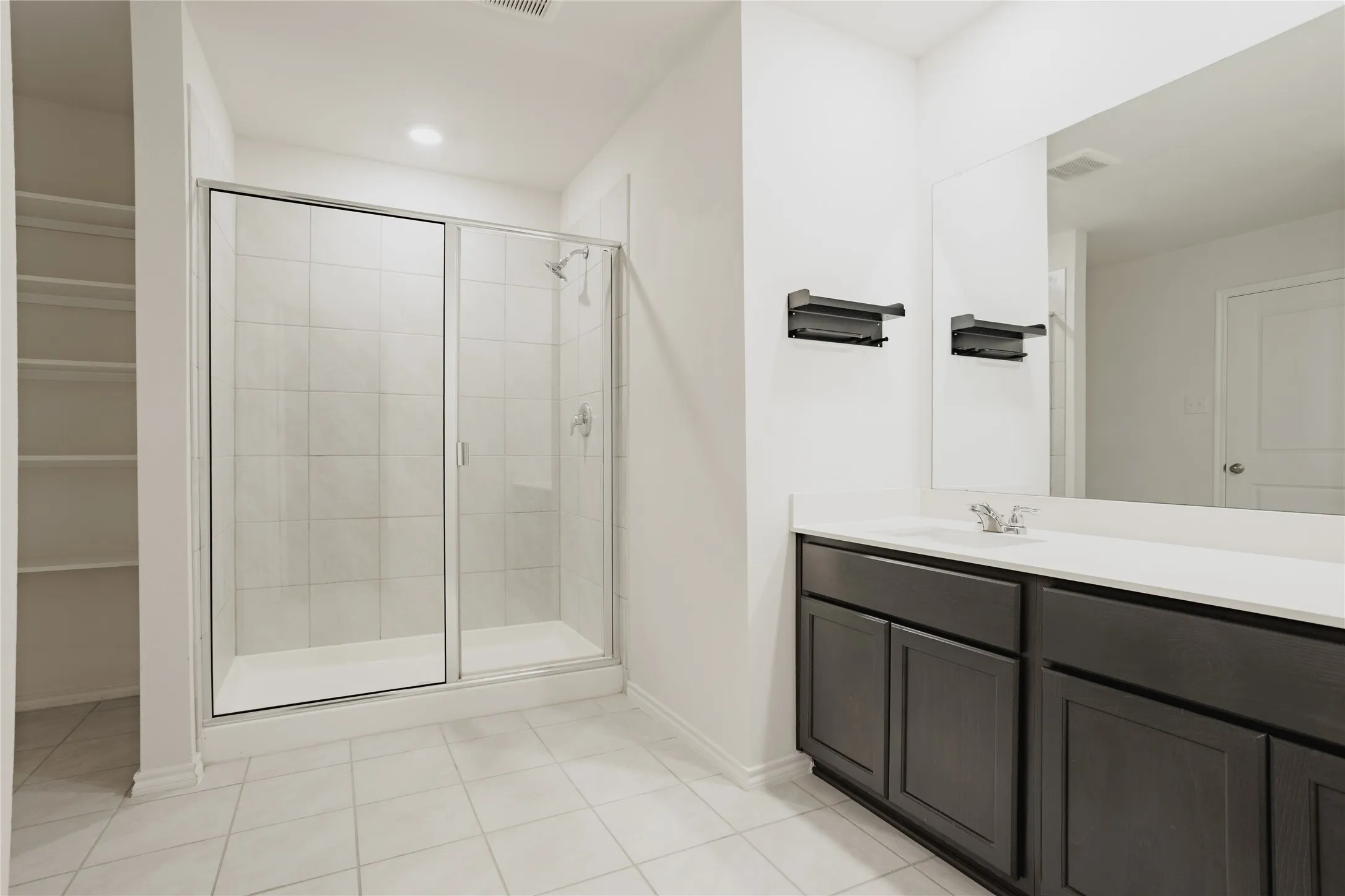 Bathroom featuring a glass-enclosed shower with tiled walls, a dark wood-finish vanity with a light-colored countertop, and a built-in shelving unit