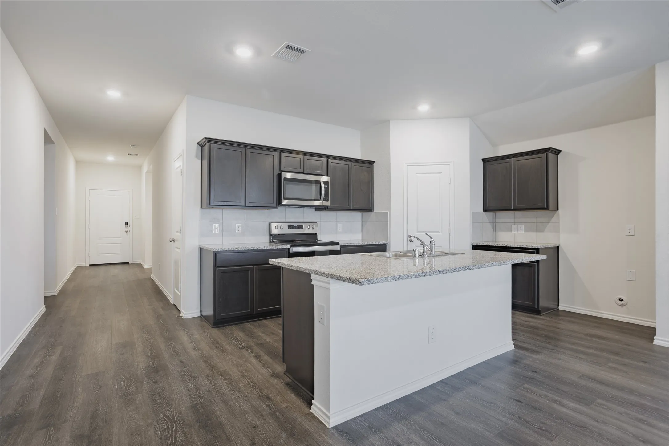 Modern kitchen featuring dark wood-finish cabinetry, stainless steel appliances, a white tile backsplash, and a central island with a light-colored countertop
