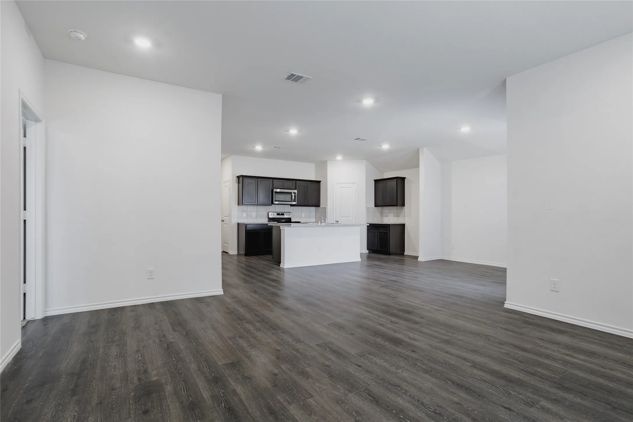 Open-concept interior featuring dark wood-finish flooring, recessed lighting, and a kitchen with dark cabinetry and stainless steel appliances