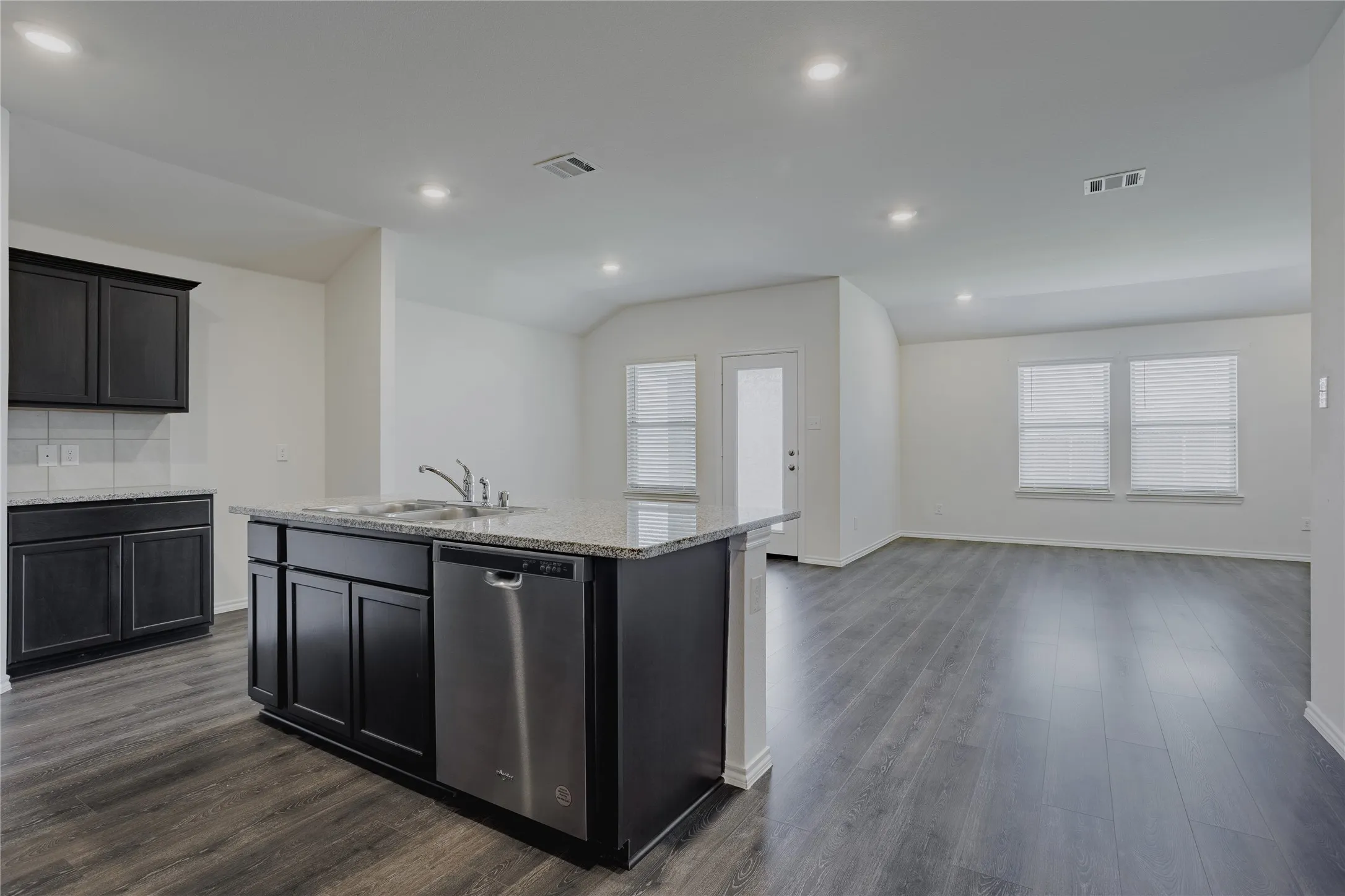 Kitchen island featuring an integrated sink, stainless steel dishwasher, and granite countertop