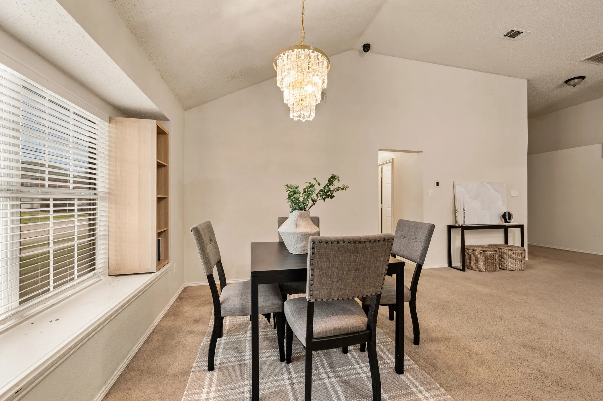 Vaulted ceiling dining area featuring a crystal chandelier, bay window with integrated shelving, and neutral carpeting
