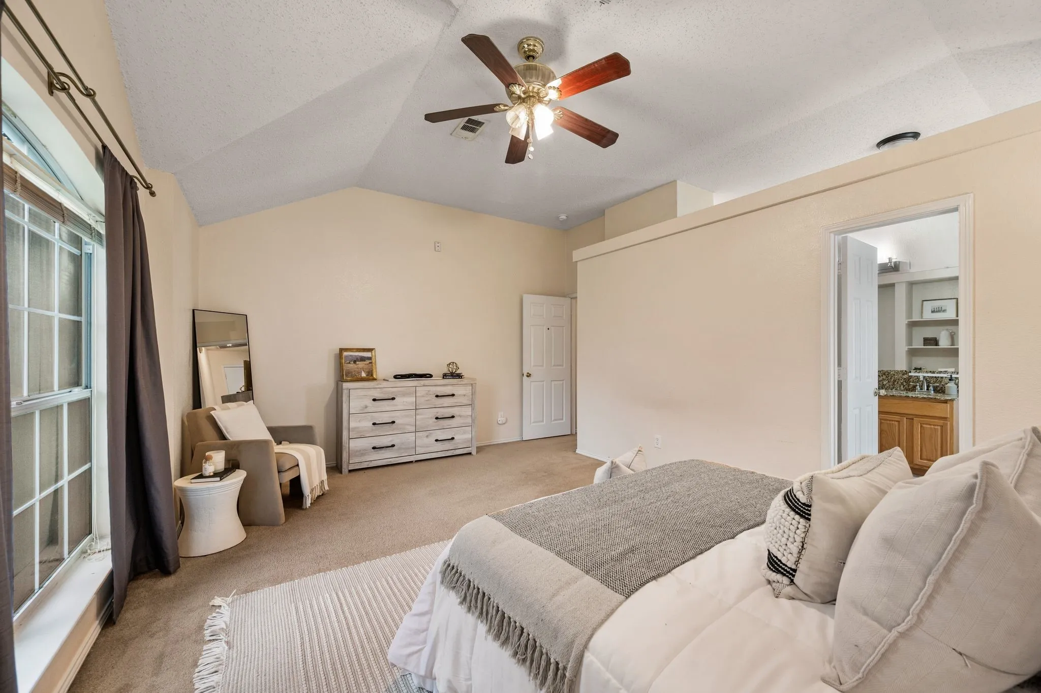 Vaulted ceilings define this carpeted room featuring a ceiling fan with light fixture