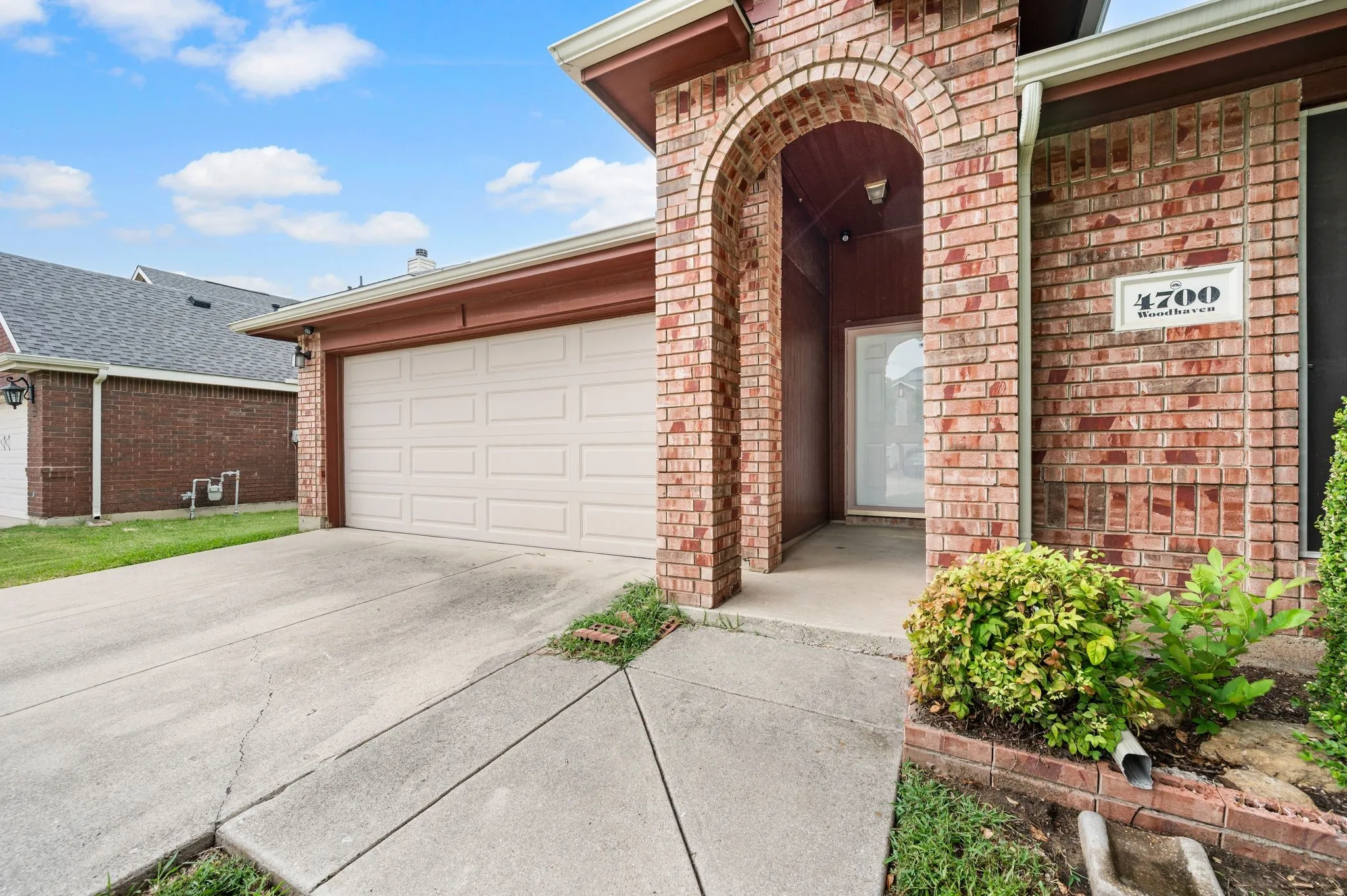 Brick facade home featuring an arched entryway, an attached garage, and a concrete driveway