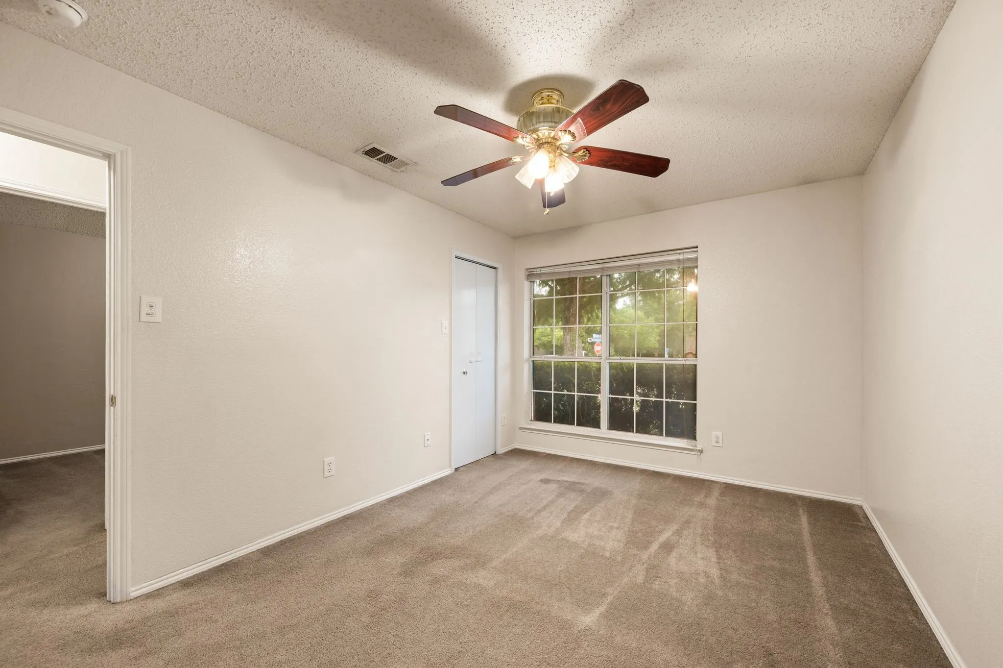 Spacious room featuring neutral carpeting, light-toned walls, and a ceiling fan with integrated lighting