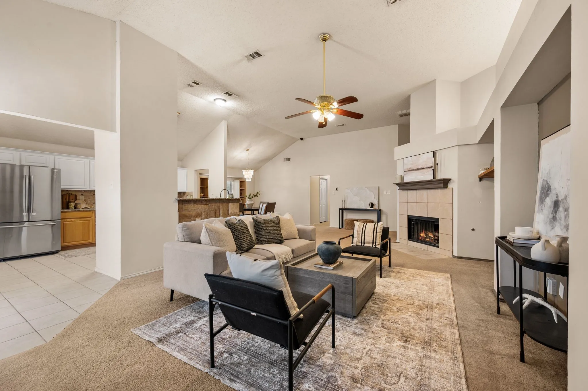 Spacious living area featuring a vaulted ceiling with a ceiling fan, a tiled fireplace with a mantel, and carpet flooring