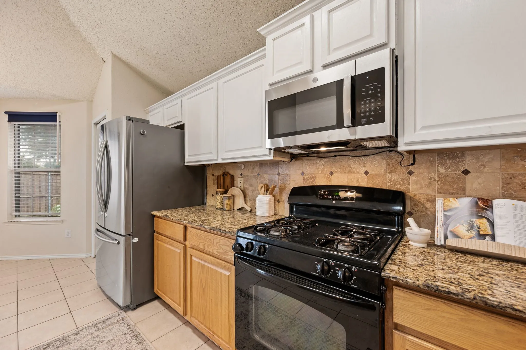 Kitchen featuring granite countertops, wood cabinetry, tile flooring, a stainless steel refrigerator, and an over-the-range microwave