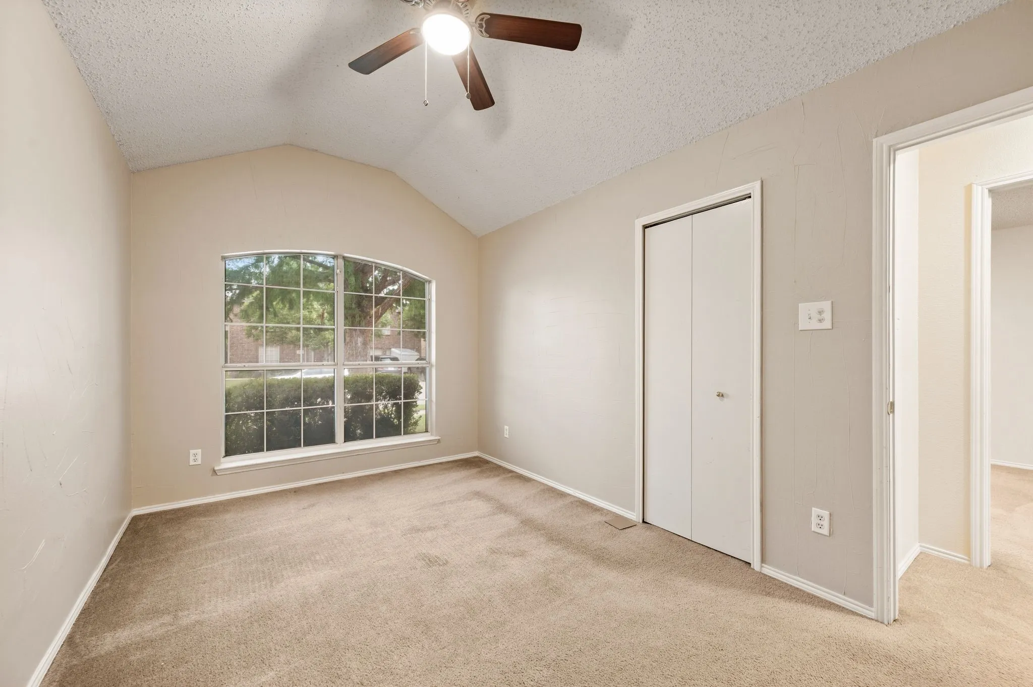 Vaulted ceiling bedroom featuring an arched window, ceiling fan, and bi-fold closet doors